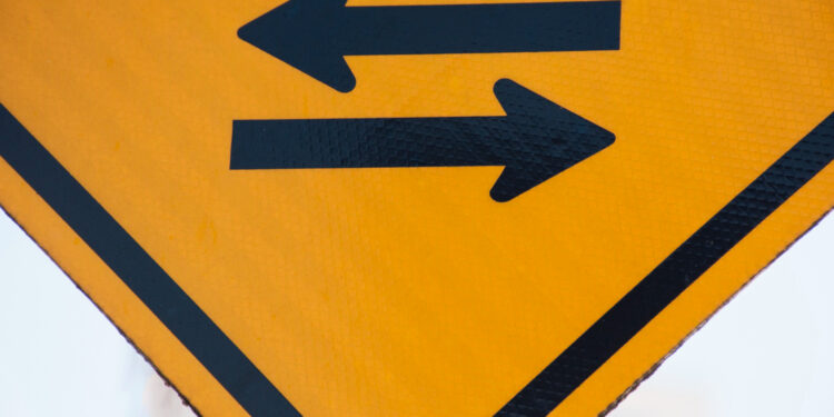 Fundo amarelo com duas setas pretas apontando para sentidos opostos: o que significa essa placa de trânsito?