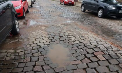 Rua pavimentada, mas cheia de buracos e com constantes alagamentos