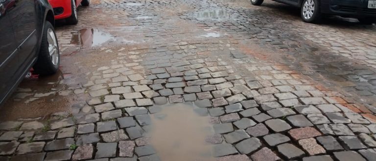 Rua pavimentada, mas cheia de buracos e com constantes alagamentos