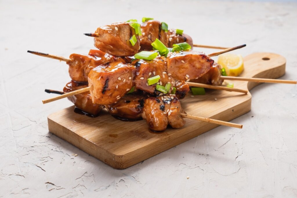 Espetinhos de frango com molho de mel em cima de uma tábua de madeira 