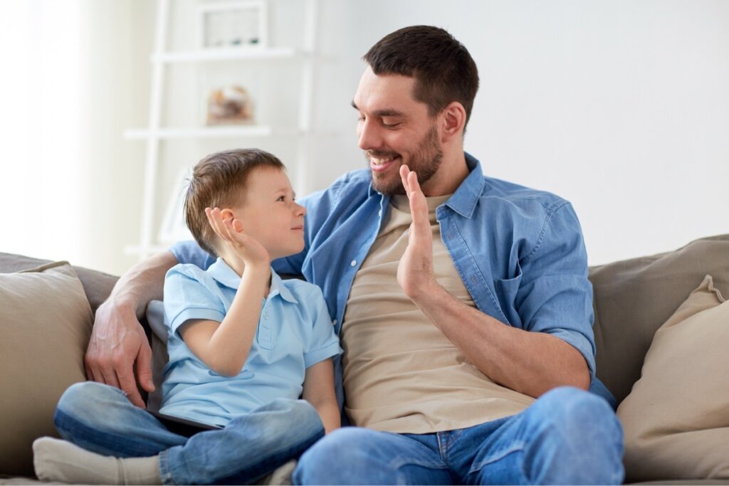 Homem e menino sentados em um sofá fazendo hi five com as mãos 