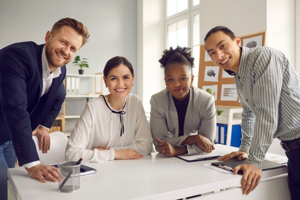 4 pessoas sorrindo reunidas ao redor de uma mesa em uma sala de reuniões