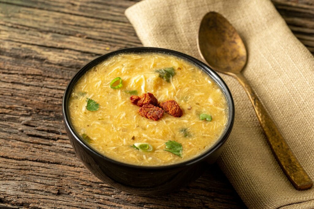 Recipiente preto com sopa de mandioquinha e frango em cima de uma mesa de madeira