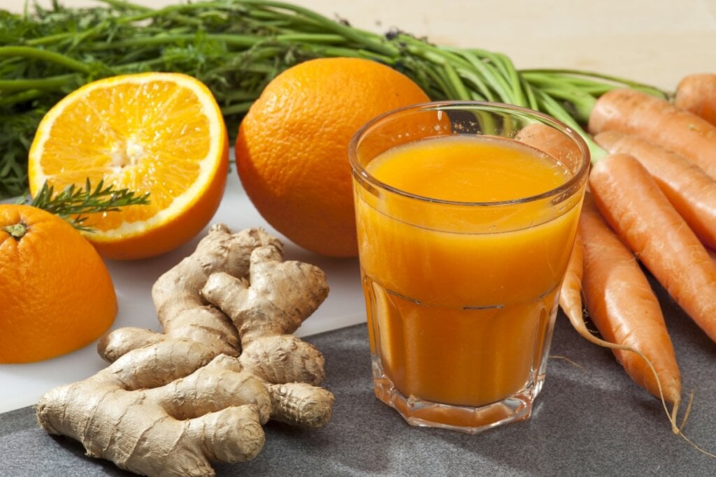 Suco de laranja, cenoura e gengibre em cima de uma mesa com  laranja, cenoura e gengibre ao lado do copo