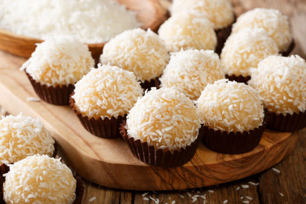 Beijinhos polvilhados com coco ralado em cima de uma tábua de madeira 