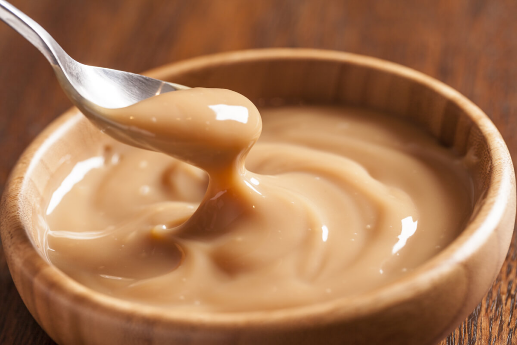 doce de leite em bowl com colher em cima de mesa de madeira