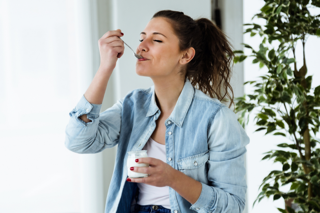 mulher comendo iogurte em sala com plantas