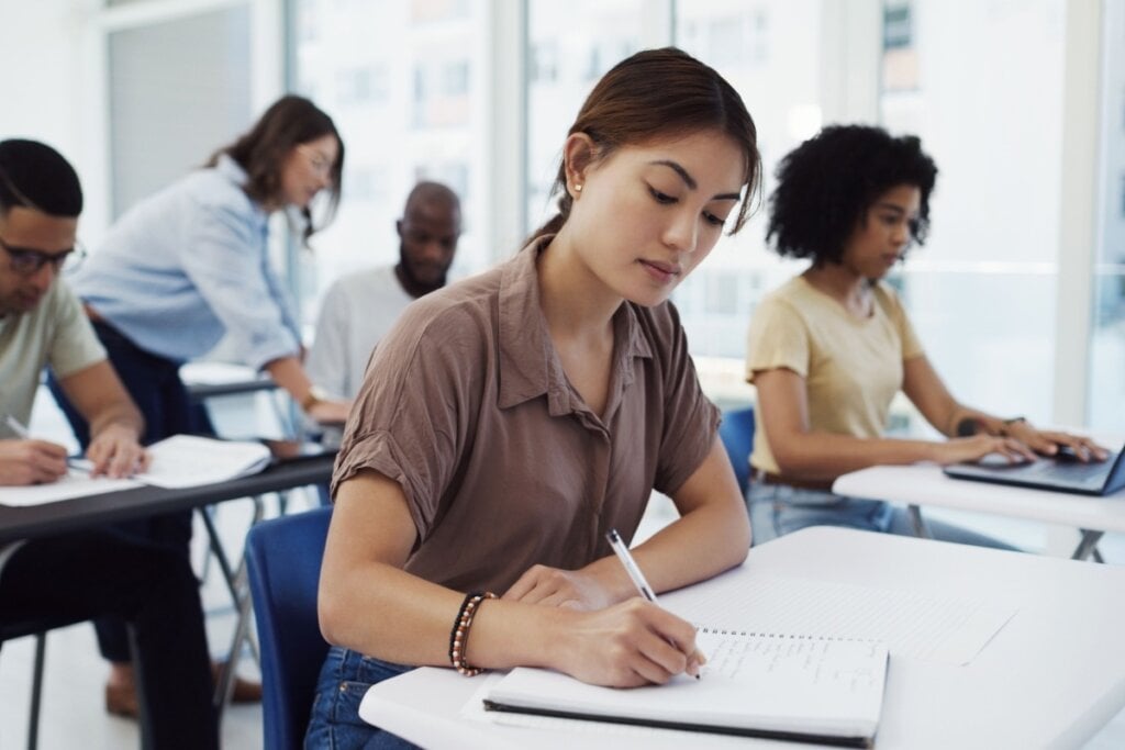 Jovem estudando em sala de aula junto a outros colegas em suas respectivas cadeiras