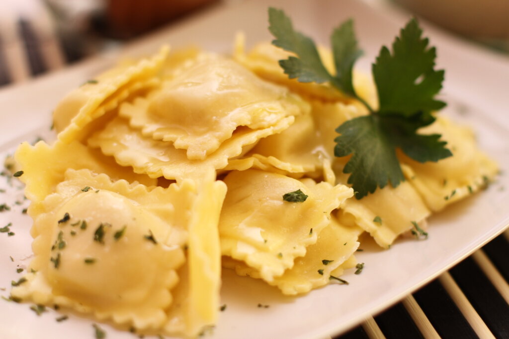 Raviolis em cima de um prato branco decorados com folha verde