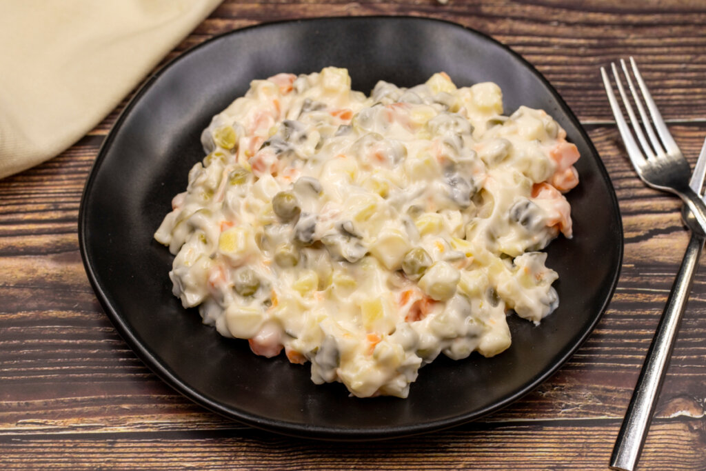 Salada de maionese com milho, ervilha e cenoura em cima de um prato preto