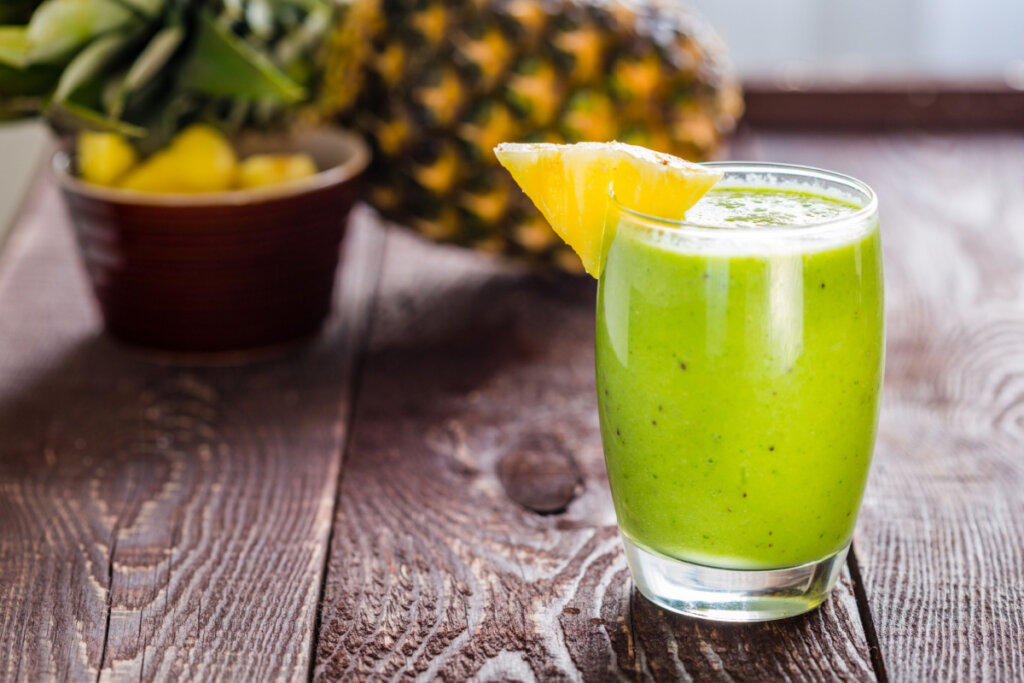 Copo de vidro com suco verde e fatia de abacaxi na borda. Abacaxi ao fundo 