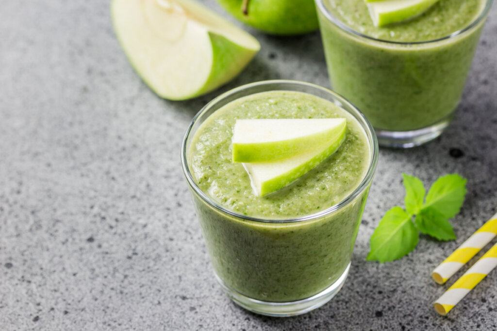 Copo de vidro com suco verde com pedaços de maçã-verde em cima