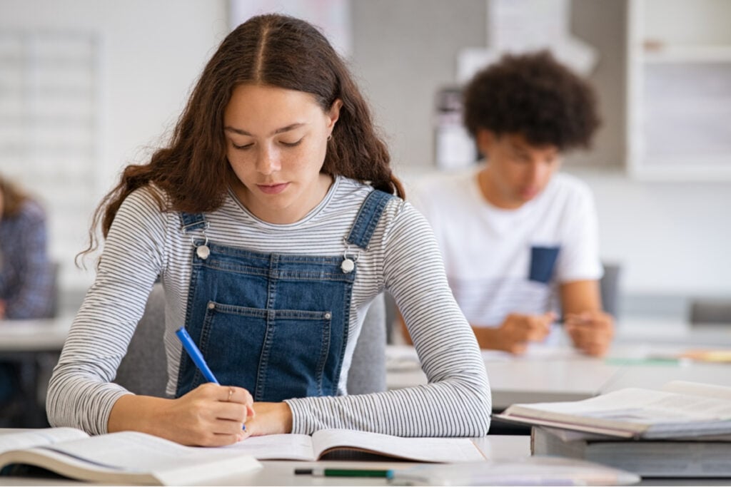 Menina sentada em sala de aula escrevendo