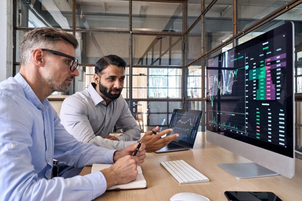 Dois homens sentados olhando para a tela de um computador com gráficos