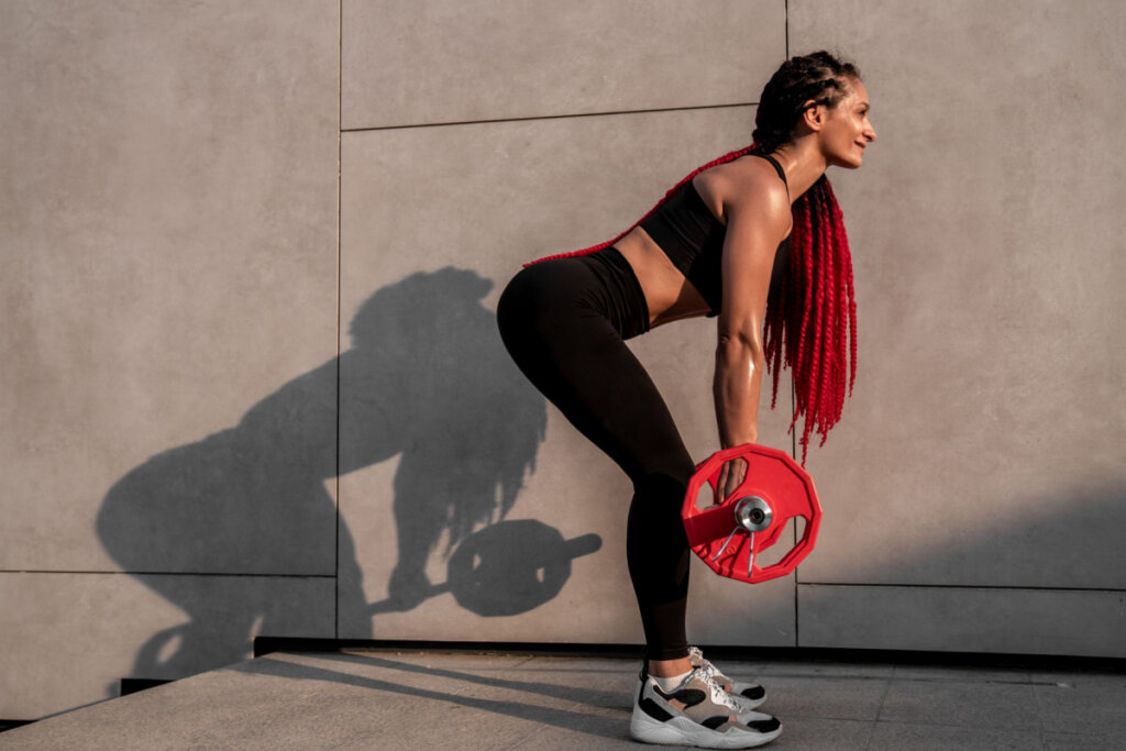 Mulher com roupa de academia levantando peso vermelho em levantamento terra