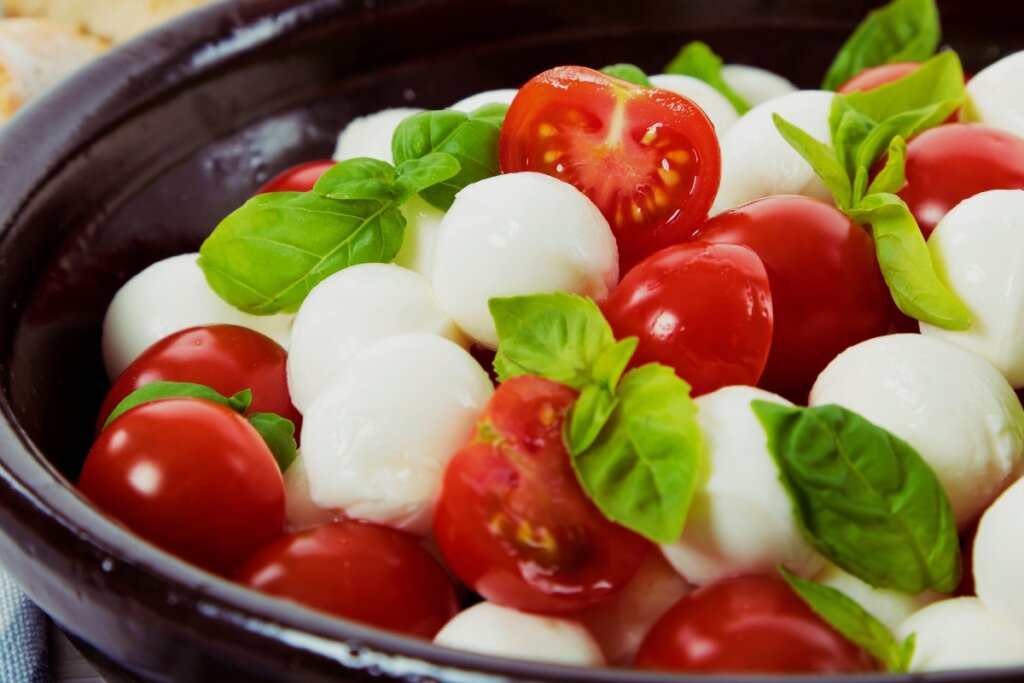 Salada Caprese composta por tomates-cereja maduros, bolinhas de mussarela de búfala e folhas frescas de manjericão