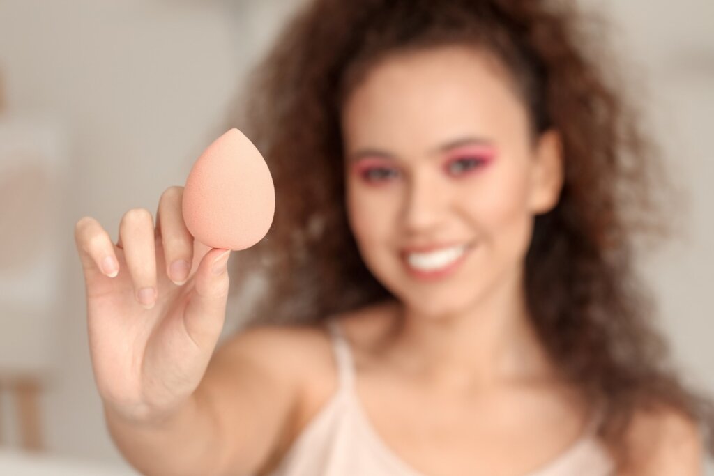 Mulher sorrindo segurando uma esponja de maquiagem na mão