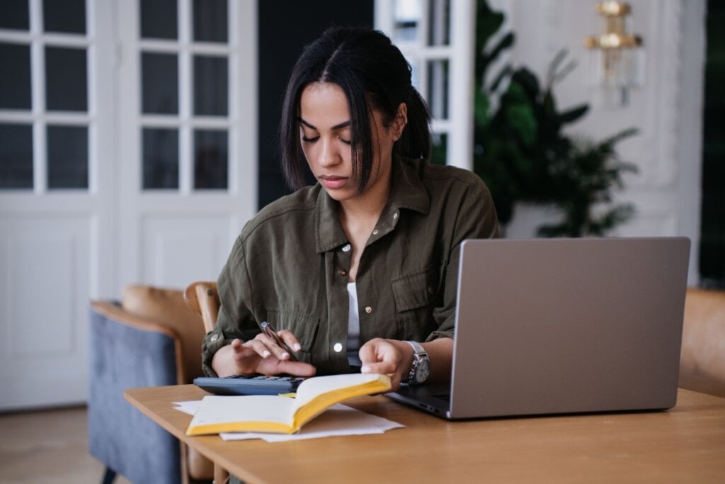 Mulher usando calculadora e anotando gastos em caderno