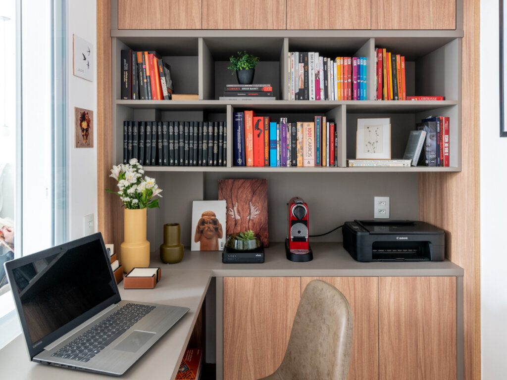 Espaço de home office médio com mesa ligada a estante e armário planejado com nichos e livros 