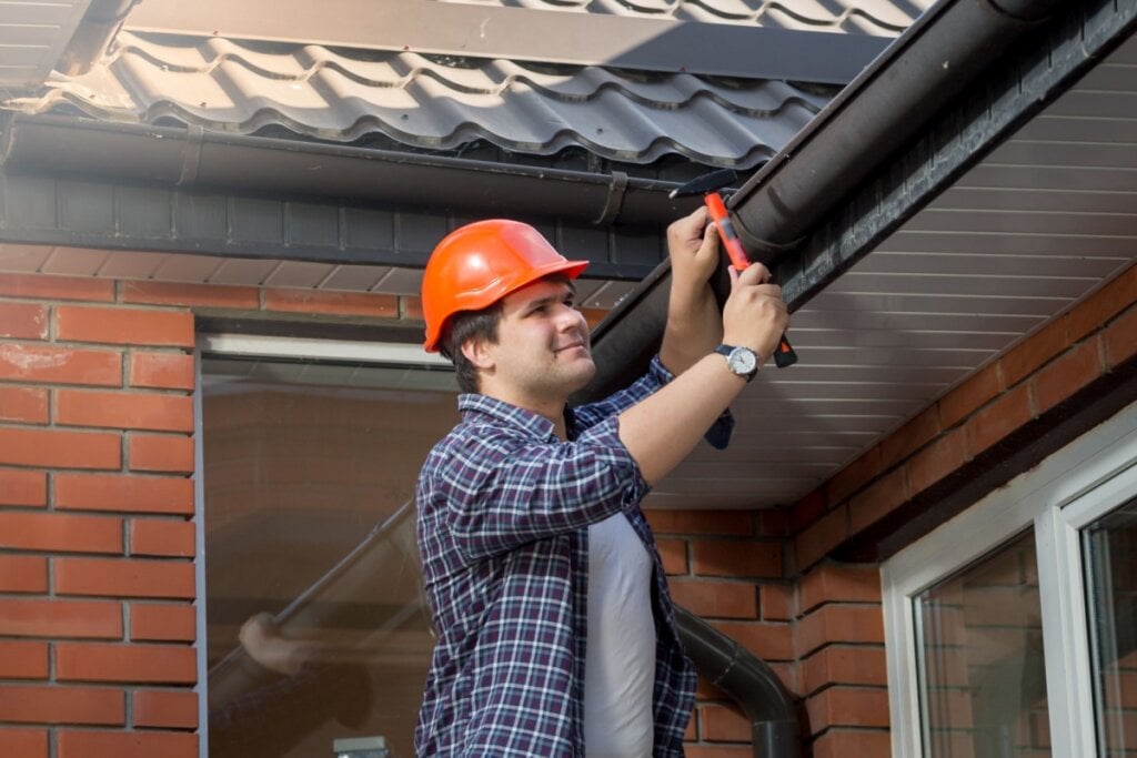 Homem de capacete vermelho martelando calha de casa