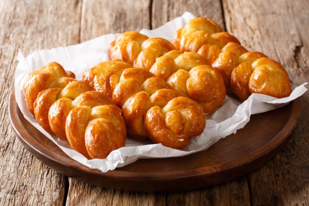 Koeksisters, doces trançados e brilhantes com calda, em cima de papel e forma de madeira