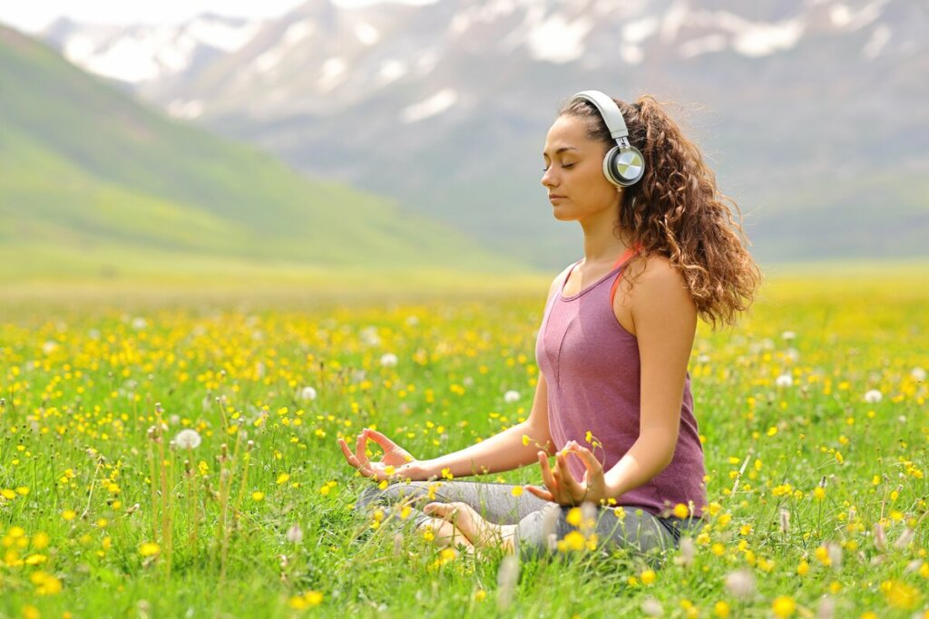 Mulher sentada em uma grama com flores usando fone e meditando