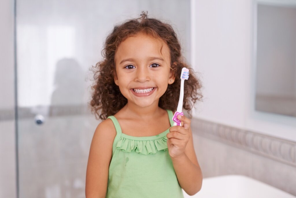 Garotinha sorrindo no banheiro com escova de dente na mão