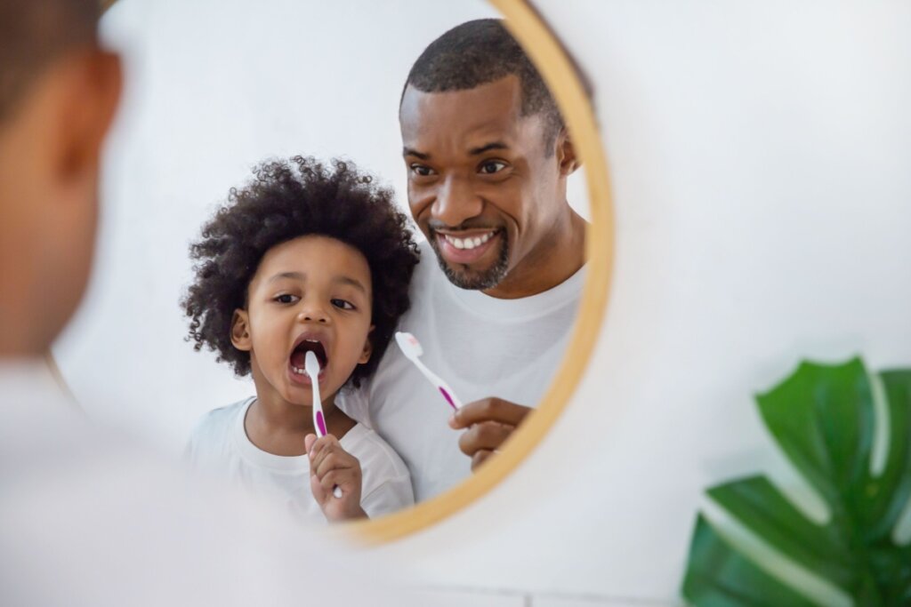 Pai ensinando o filho a escovar o dente na frente do espelho