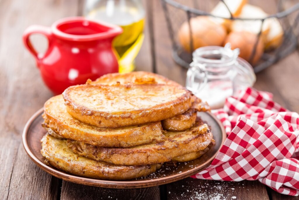 Fatias de rabanada servidas em prato de cerâmica em cima de uma mesa de madeira