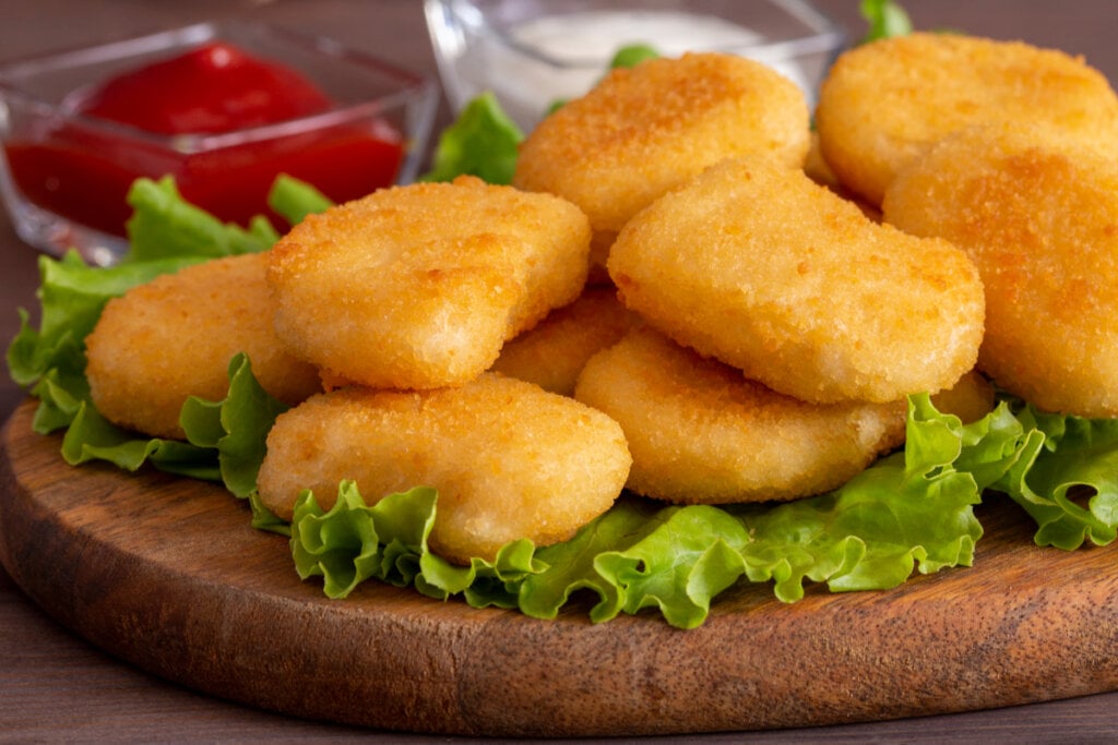 Nuggets em cima de tábua com alface e molhos acompanhando.