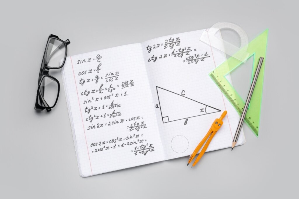 Caderno aberto com anotações e fórmulas de trigonometria ao lado de um compasso, régua triangular e óculos