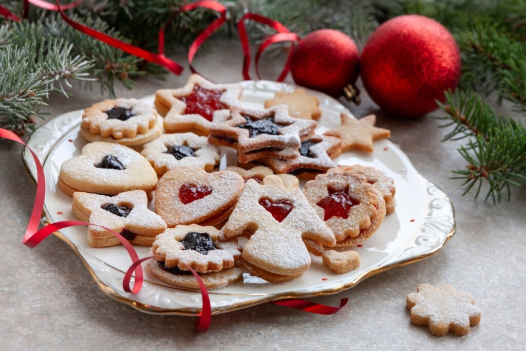 Biscoitos em prato branco com bordas douradas ao lado de galhos de árvore e bolas natalinas