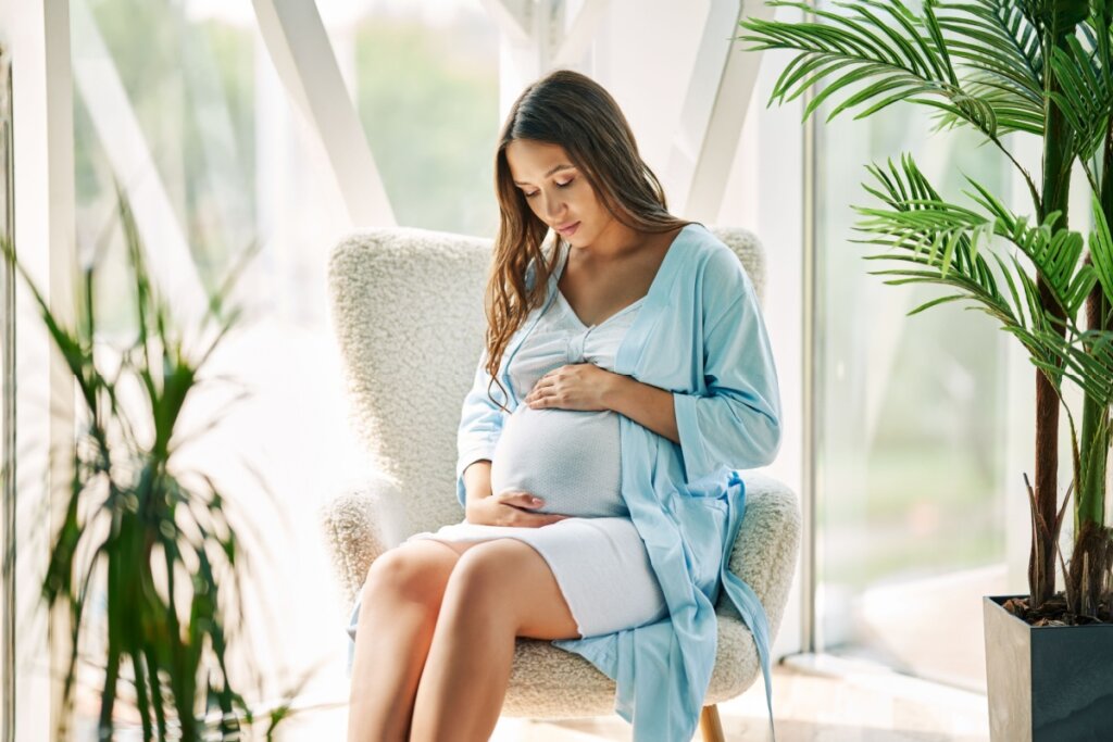 Mulher grávida sentada em sofá branco segurando a sua barriga