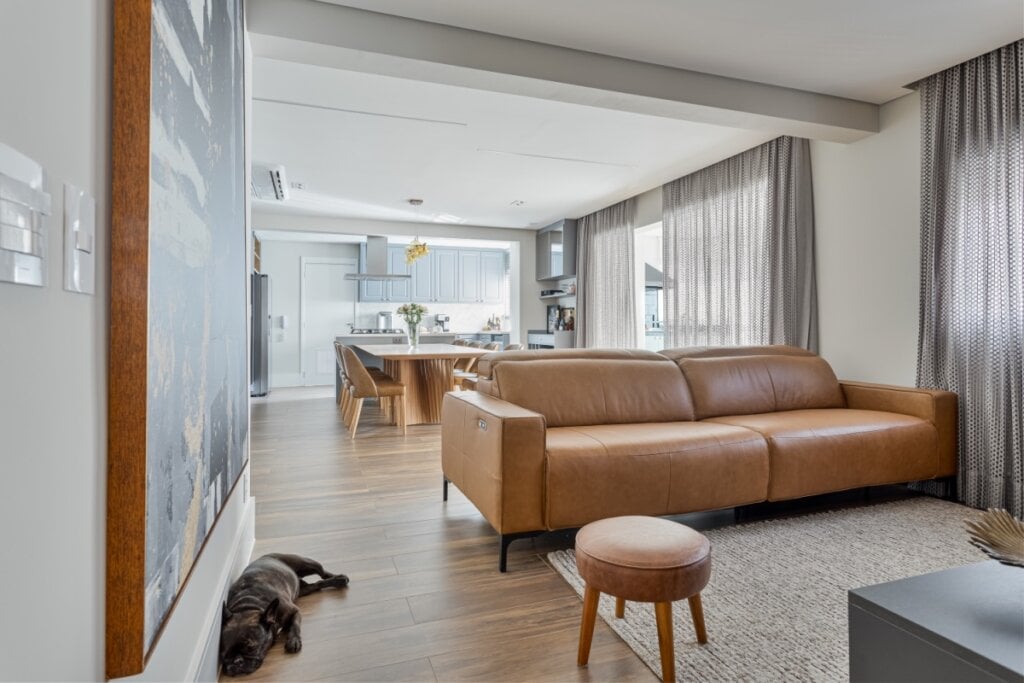 Sala de estar com sofá marrom, combinando com cortinas cinza e uma mesa de jantar ao fundo