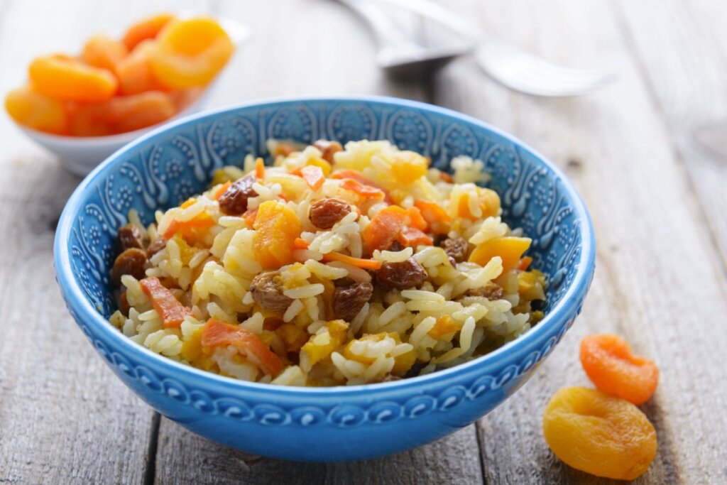 Arroz com frutas secas servido em cumbuca de cerâmica azul em cima de mesa de madeira