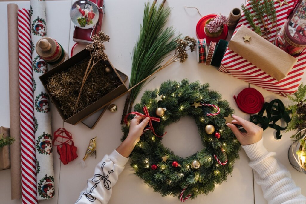 duas mãos colocando enfeites em guirlanda verde e elementos ligados ao natal em volta