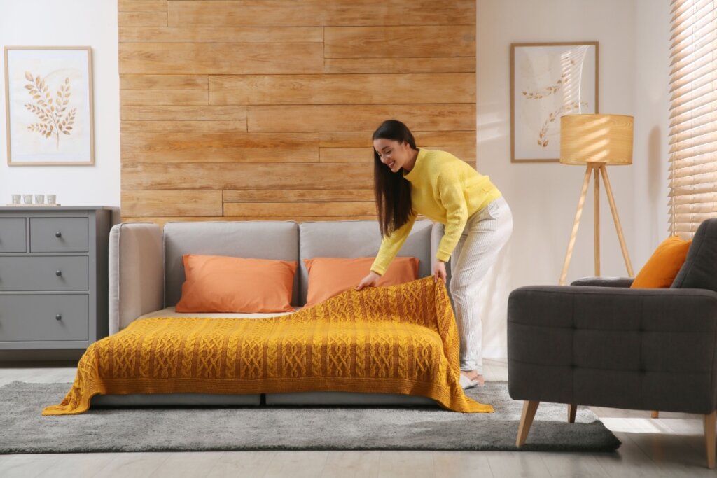 Uma mulher arrumando um sofá-cama em uma sala iluminada e aconchegante