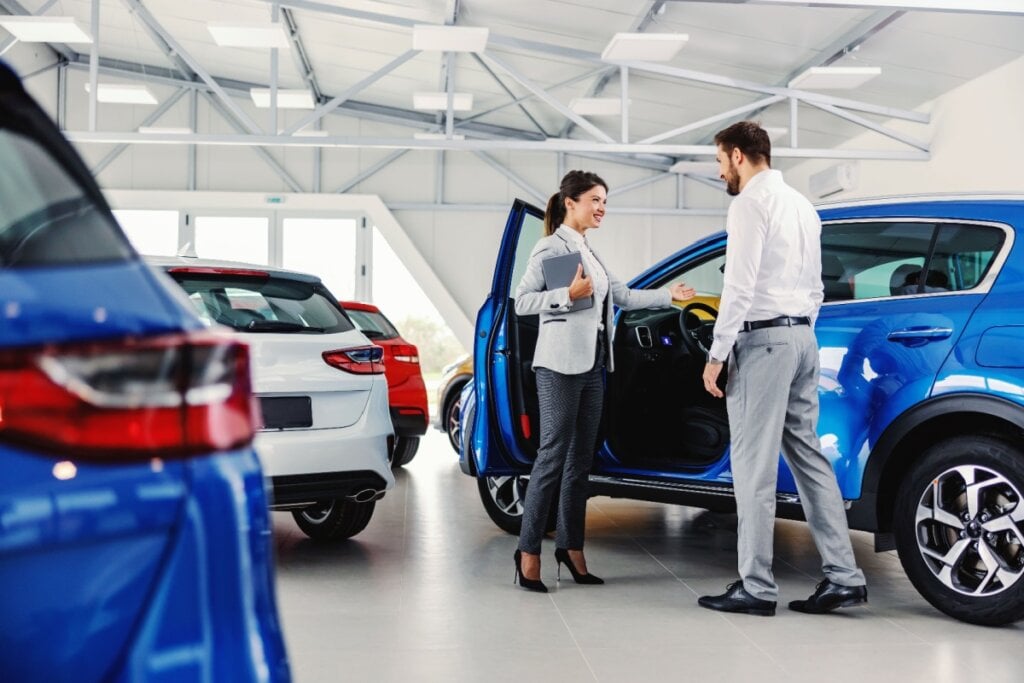 Mulher bem vestida apresentando um carro azul a um cliente em uma concessionária